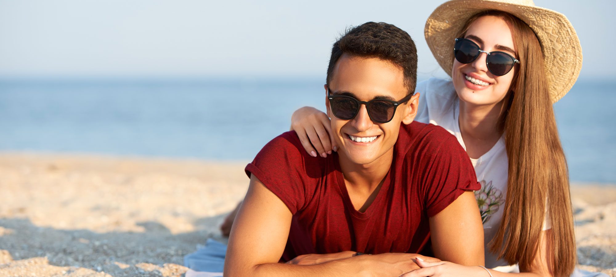 A young couple laying on the beach smiling at the camera