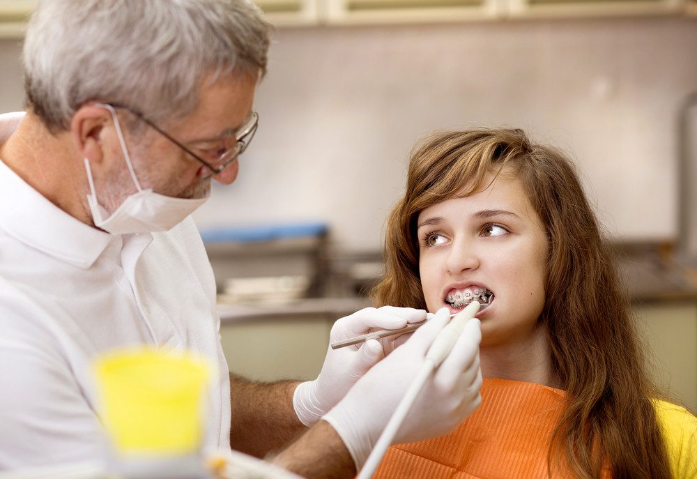 Teenage girl with the braces on her teeth is having a treatment at dentist